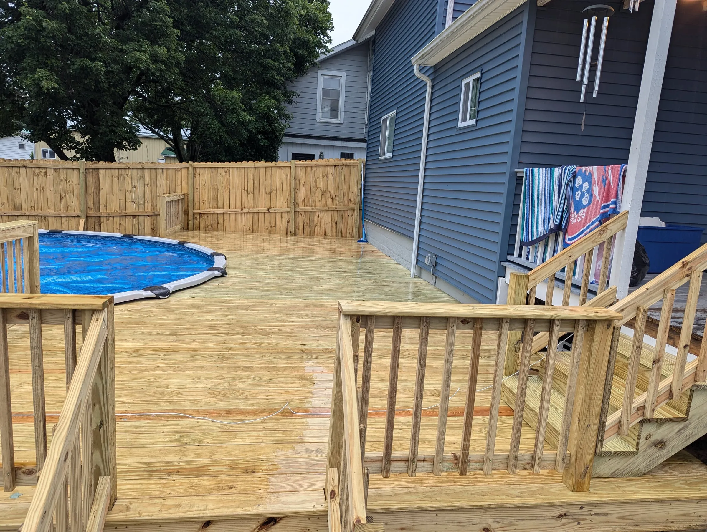 Finished pressure-treated deck wrapping an above-ground pool, with railings and stairs