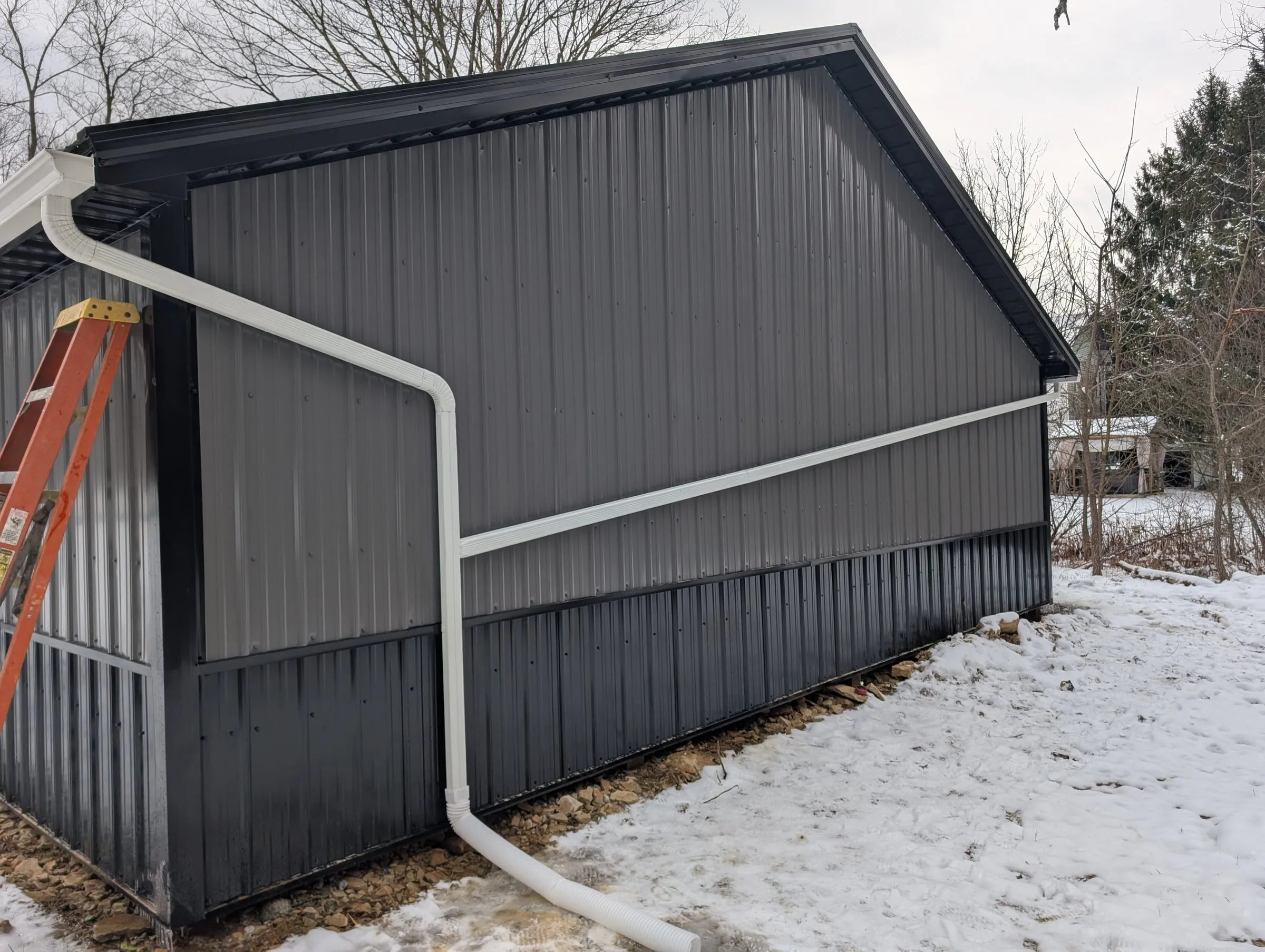 Side of the garage in snow showing white gutters and a downspout on the steel siding